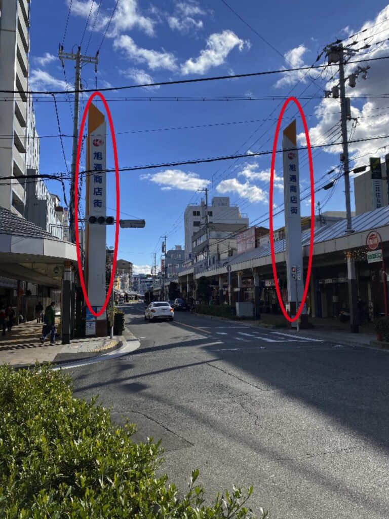 ロータリーを出ると「旭通商店街」と書かれた大きな２本の柱が立つ三差路があります。