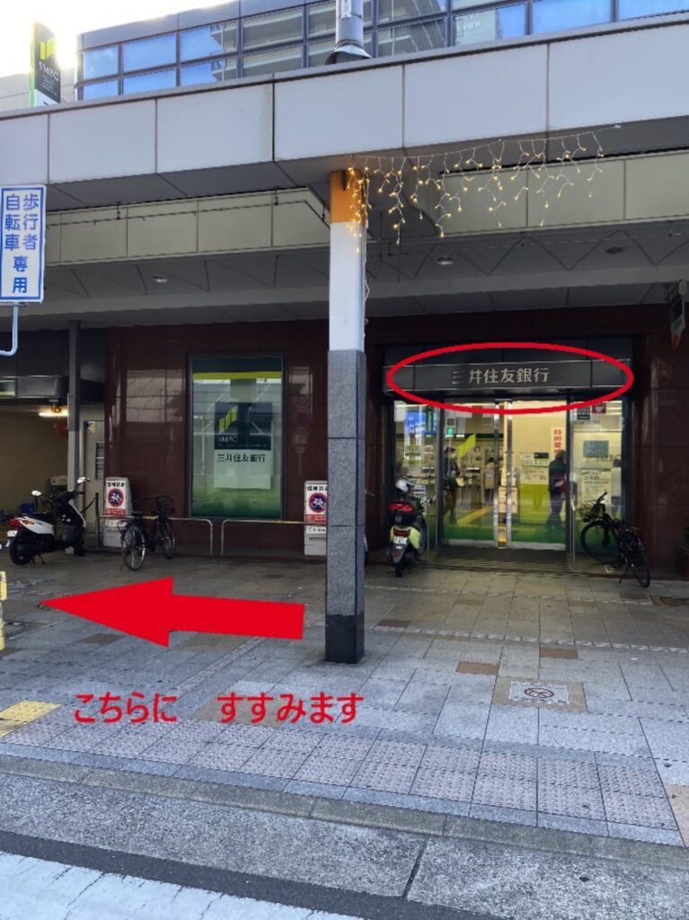 その三差路を「三井住友銀行」がある方へ渡ります。 そして、駅を背にして商店街方面へ歩いて行きます。